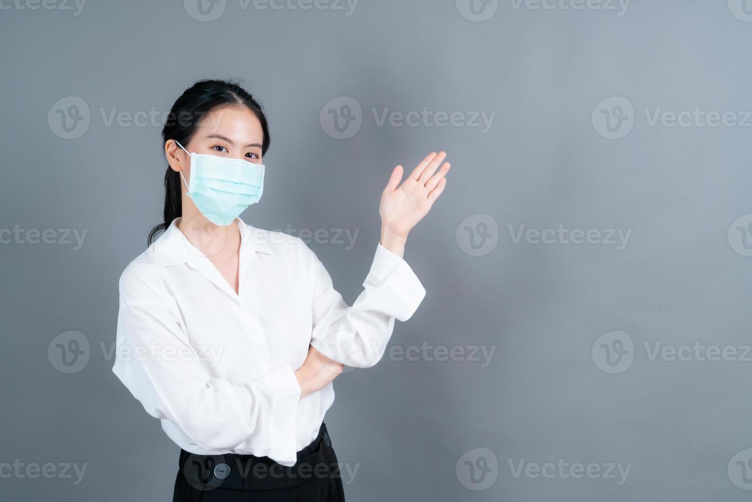 asiatische frau, die eine medizinische gesichtsmaske trägt, schützt filterstaub pm2.5 gegen verschmutzung, antismog und covid-19 mit handpräsentation foto