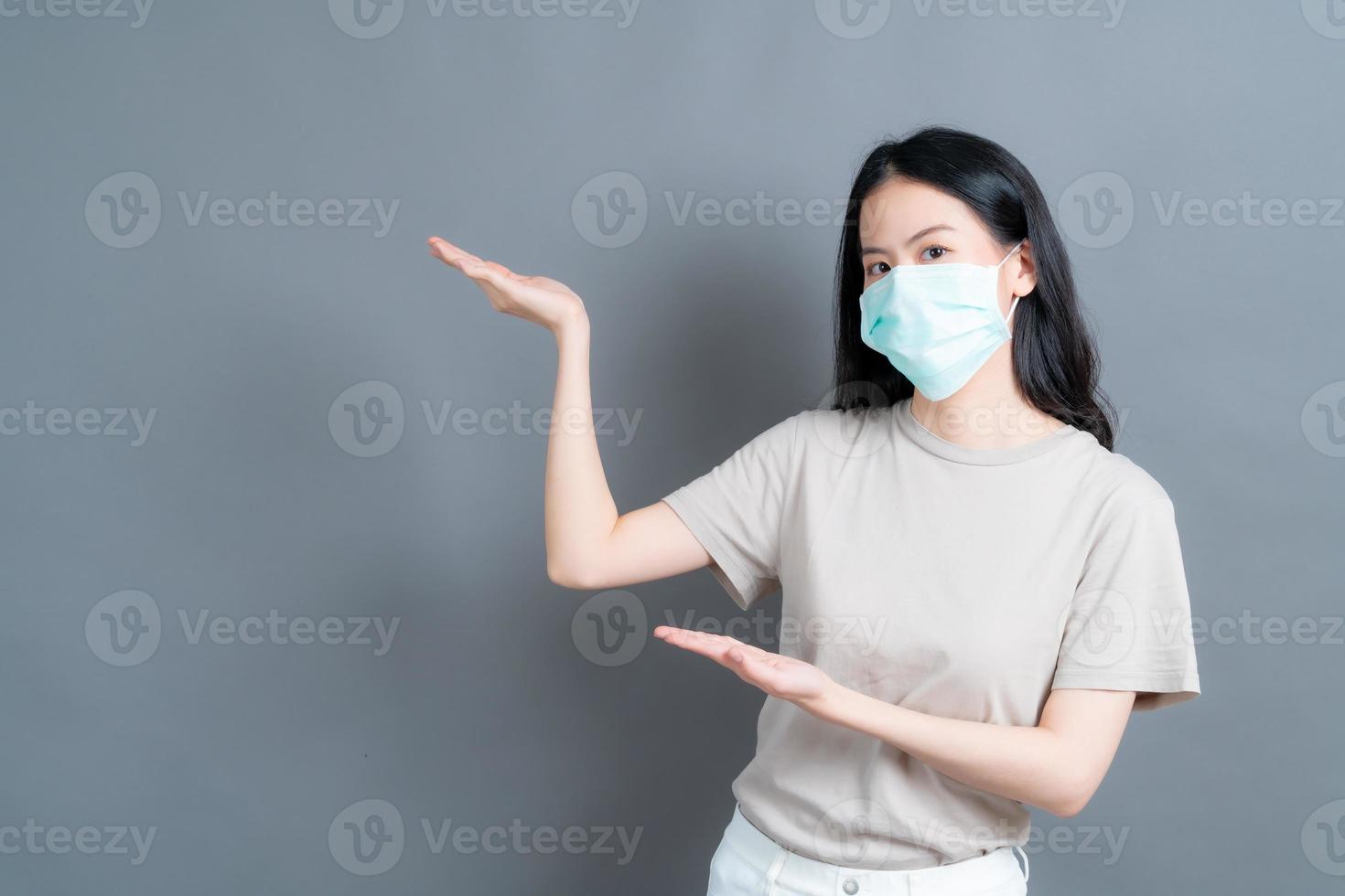 asiatische frau, die eine medizinische gesichtsmaske trägt, schützt filterstaub pm2.5 gegen verschmutzung, antismog und covid-19 mit handpräsentation foto