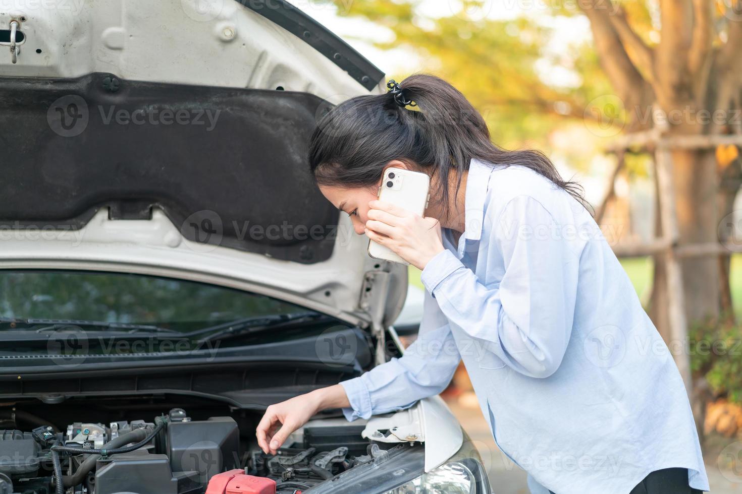 Junge Frau, die in der Nähe eines kaputten Autos mit aufgeklappter Motorhaube steht und Probleme mit ihrem Fahrzeug hat foto