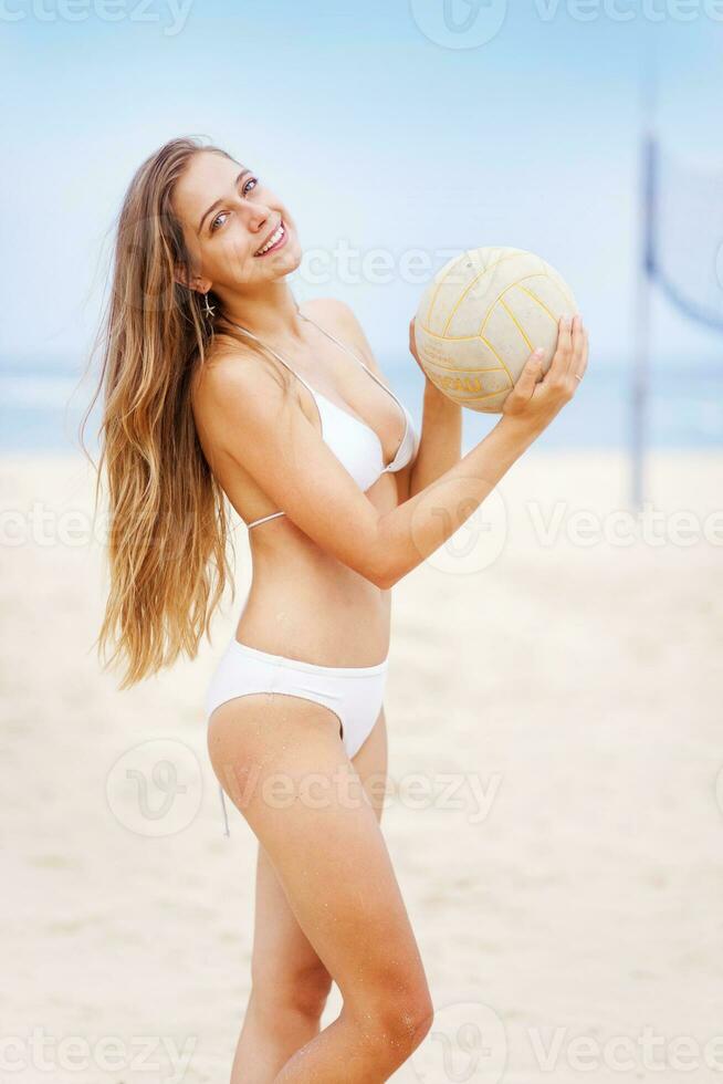 ein Frau im ein Weiß Bikini halten ein Volleyball foto