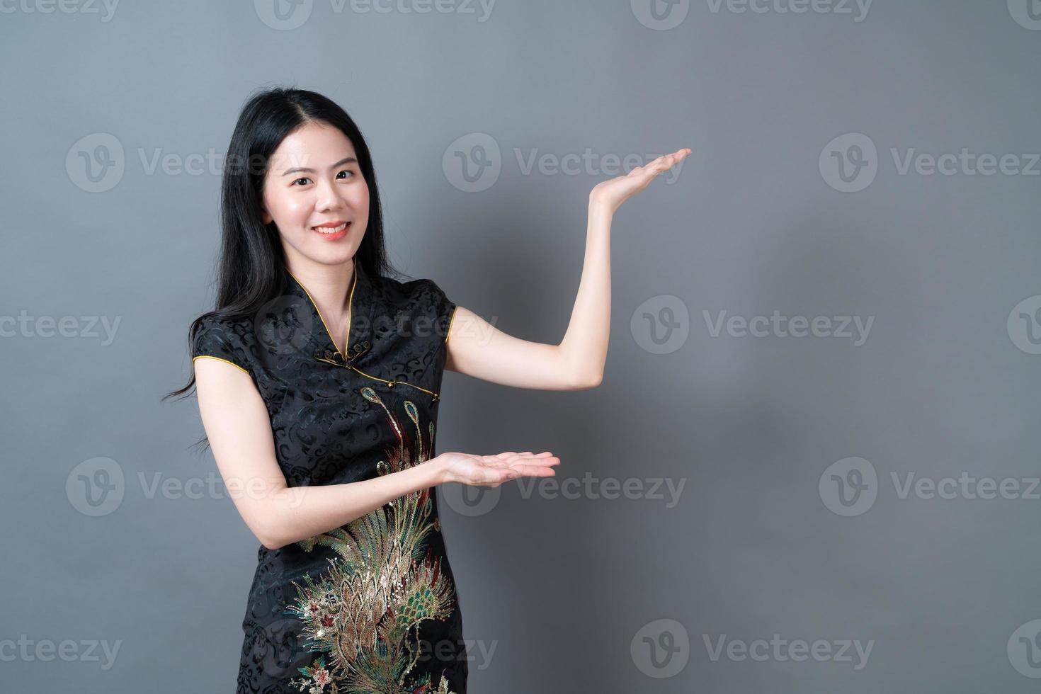 schöne junge asiatische frau trägt chinesisches traditionelles kleid mit der hand, die auf der seite präsentiert foto