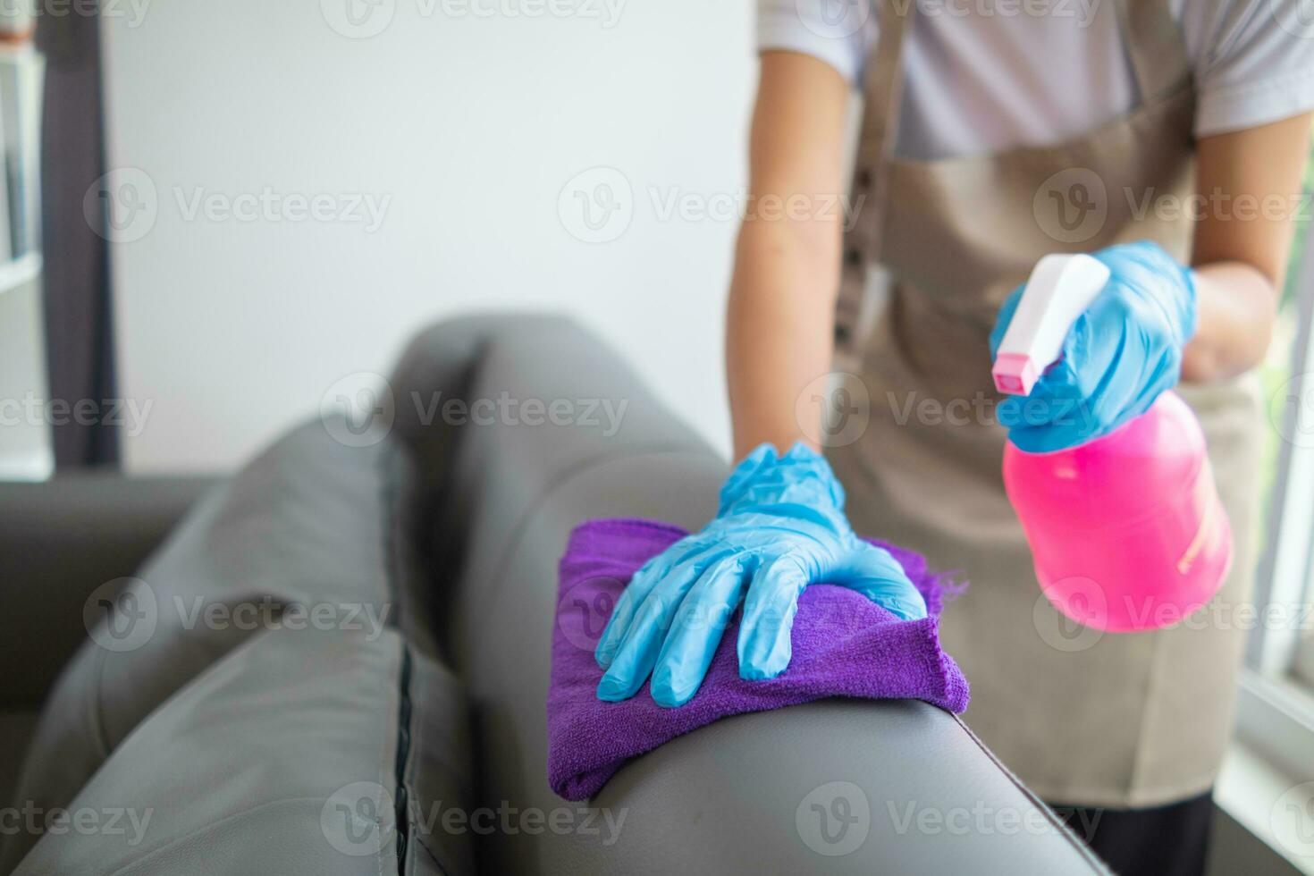 Reinigung Mitarbeiter ist abwischen Stoff mit Reiniger und Desinfektionsmittel auf das Oberfläche von Sofa zu machen das Sofa sauber mit Reinigung Produkte und kostenlos von Keime klammern zu Oberfläche von das Sofa im Leben Zimmer. foto