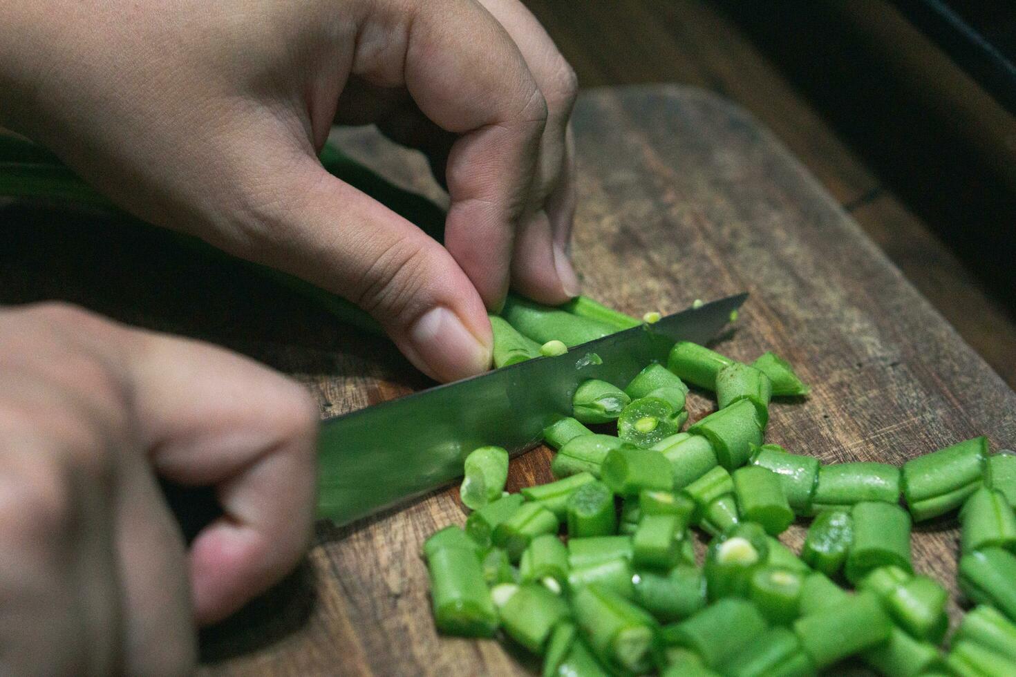 Foto von weiblich Hand Hacken Grün Bohnen auf hölzern Schneiden Tafel zum Kochen