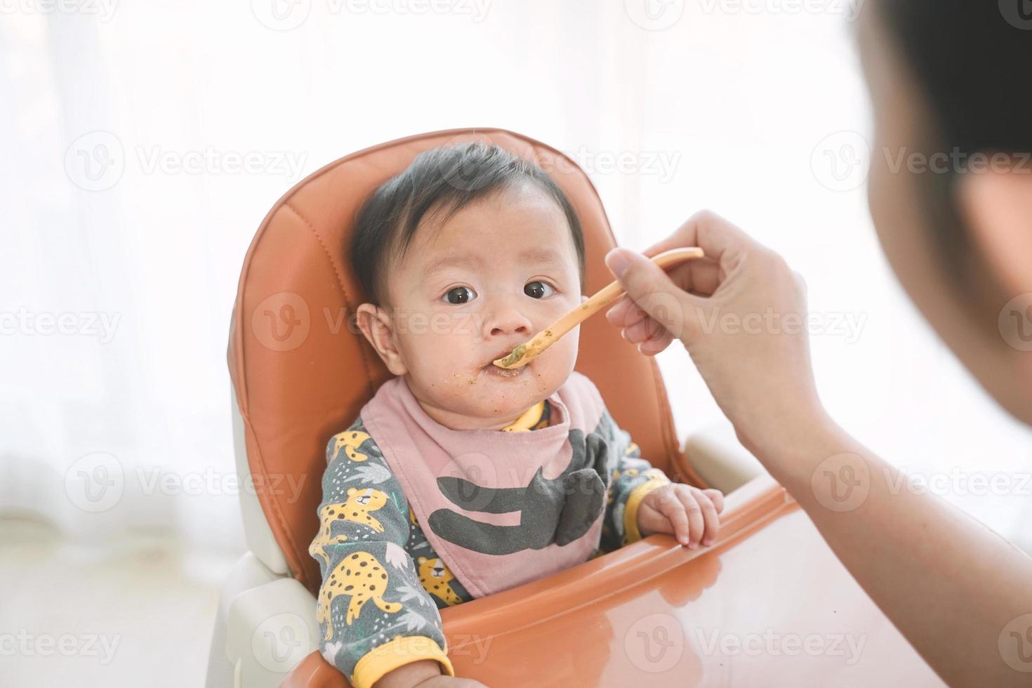 6 Monate altes Baby, das Essen auf einem Hochstuhl mischt. foto