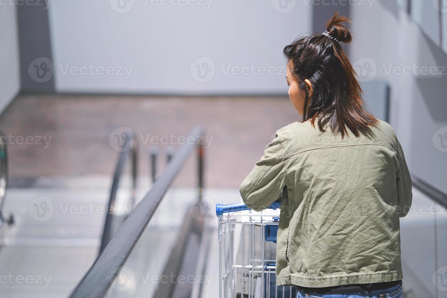 Frau mit Einkaufswagen auf Rolltreppe im Megastore. foto