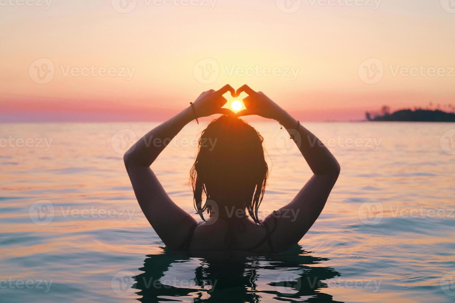 Rückansicht der asiatischen Frau, die Herzzeichen im Meer macht. Urlaubsvitalität gesundes Wohnkonzept. Silhouette Hand in Herzform. foto