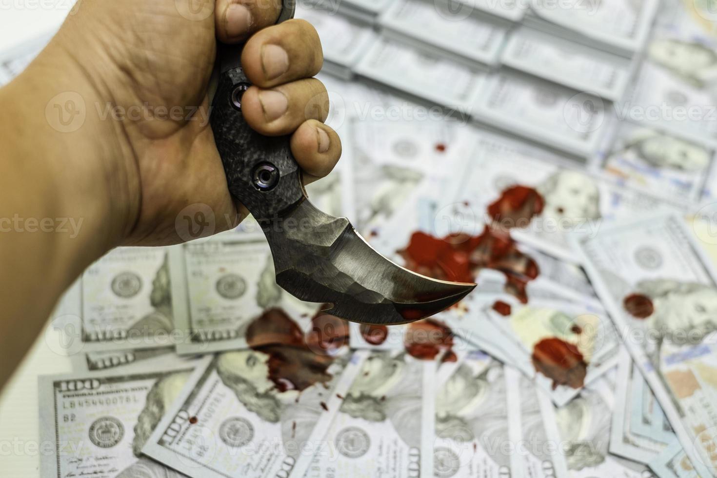 Hand, die Karambit-Messer auf Stapelbündeln von 100-US-Dollar-Banknoten blutig hält foto