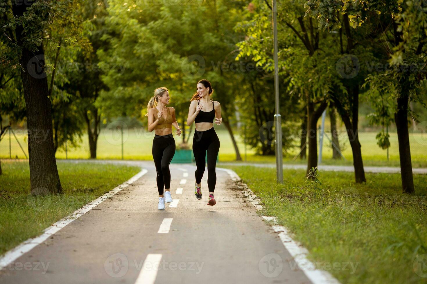 zwei ziemlich jung Frauen Laufen auf das Fahrbahn im das Park foto