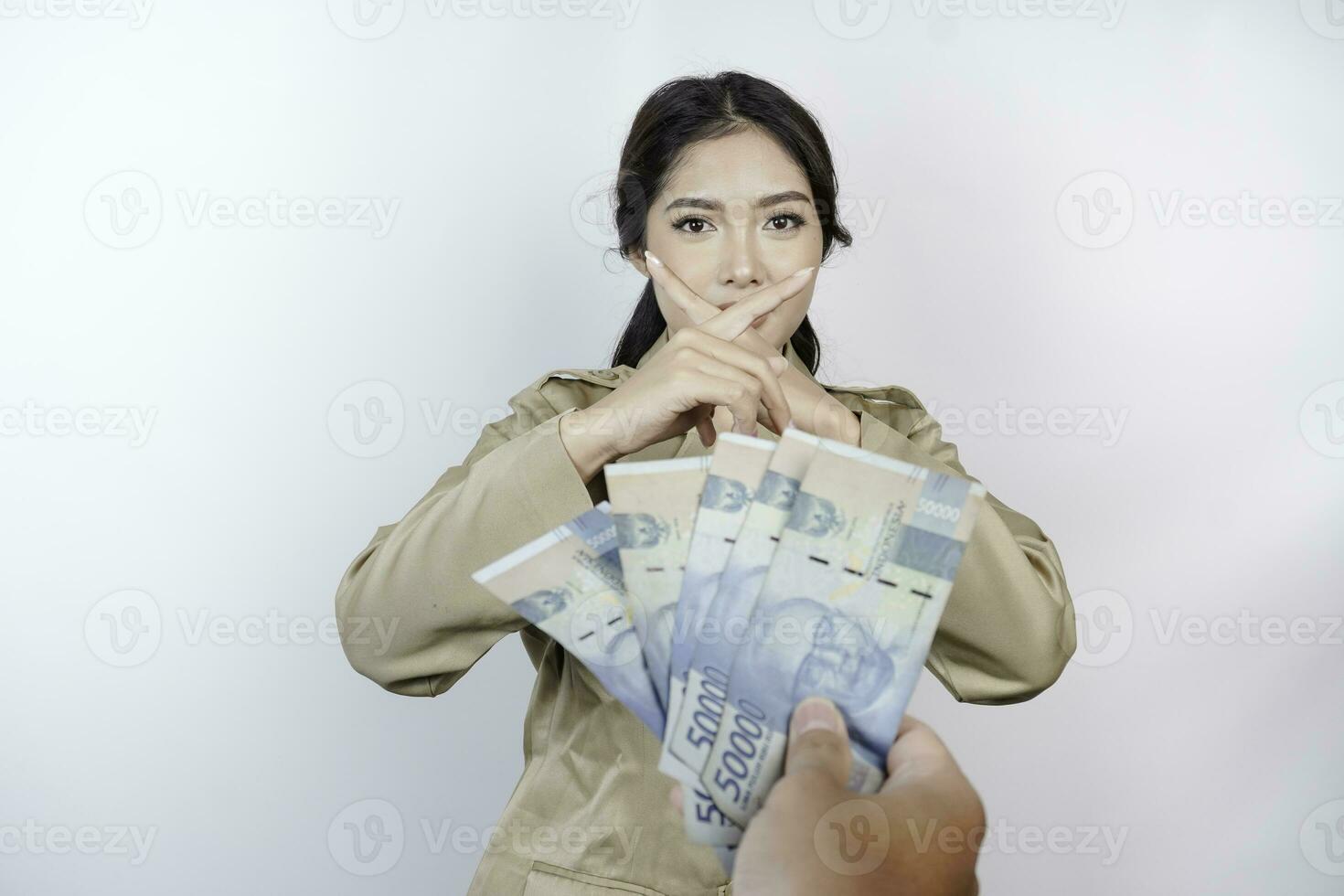 ein ernst jung Regierung Arbeiter Frau ist tragen khaki Uniform gestikulieren Ablehnung zu Kasse Geld im indonesisch Rupiah isoliert durch Weiß Hintergrund foto