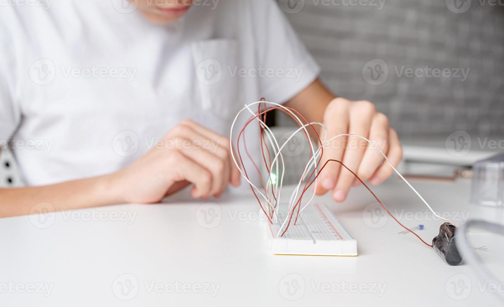 Junge, der mit LED-Leuchten auf Experimentiertafel für Wissenschaftsprojekt arbeitet foto