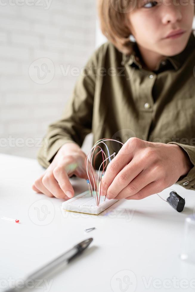 Junge, der mit LED-Leuchten auf Experimentiertafel für Wissenschaftsprojekt arbeitet foto