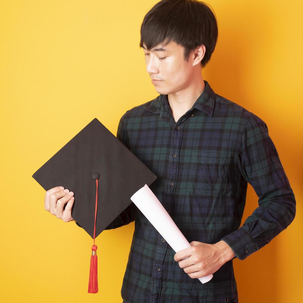 Universitätsmann ist glücklich mit Abschluss auf gelbem Hintergrund foto