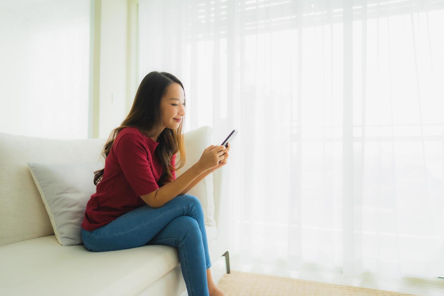 Portrait schöne junge asiatische Frauen mit Handy oder Smartphone auf dem Sofa foto