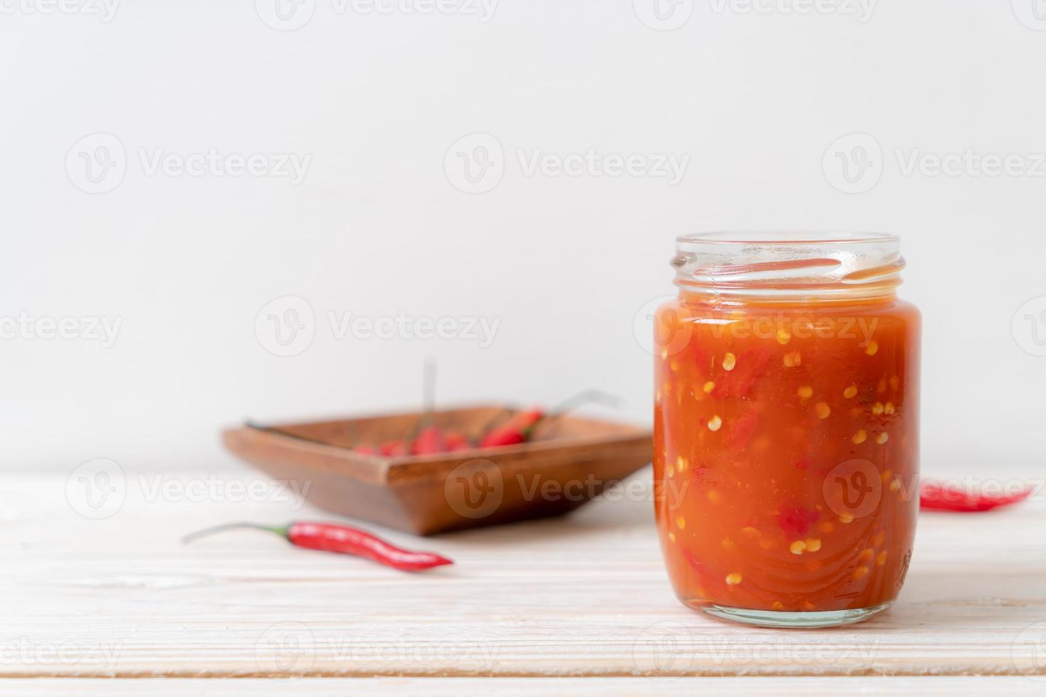 Chili oder Chilisauce in Flasche und Glas auf Holzhintergrund on foto