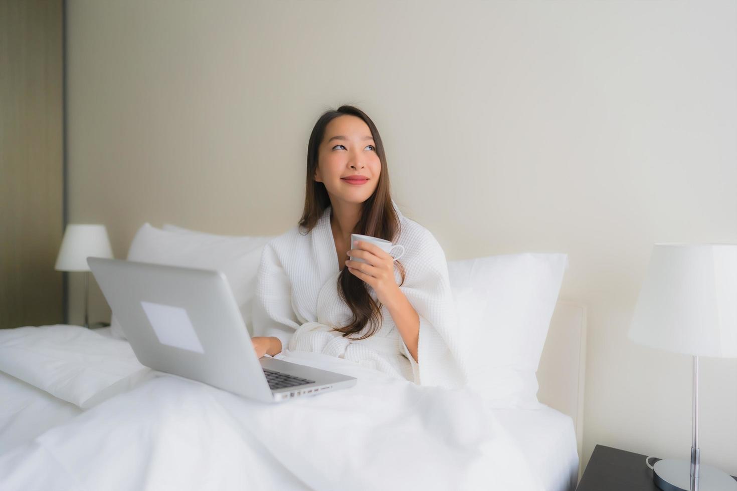 Porträt schöne junge asiatische Frauen mit Kaffeetasse und Computer-Laptop auf dem Bett foto