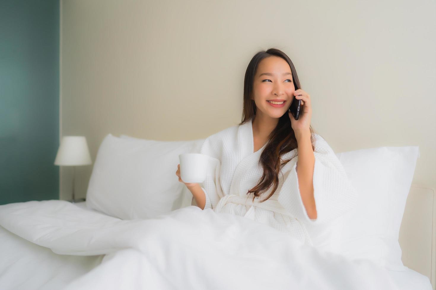 Porträt schöne junge asiatische Frauen mit Kaffeetasse und Handy auf dem Bett foto