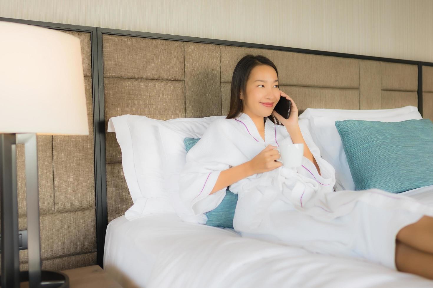 Porträt schöne junge asiatische Frauen mit Handy Smartphone mit Kaffeetasse auf dem Bett foto