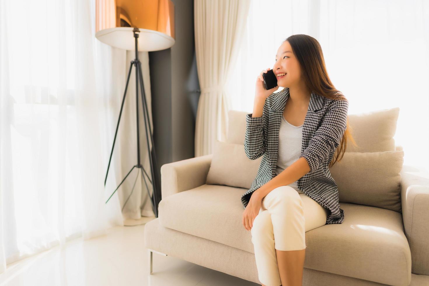 Porträt schöne junge asiatische Frauen mit sprechendem Handy und sitzen auf Sofasessel foto