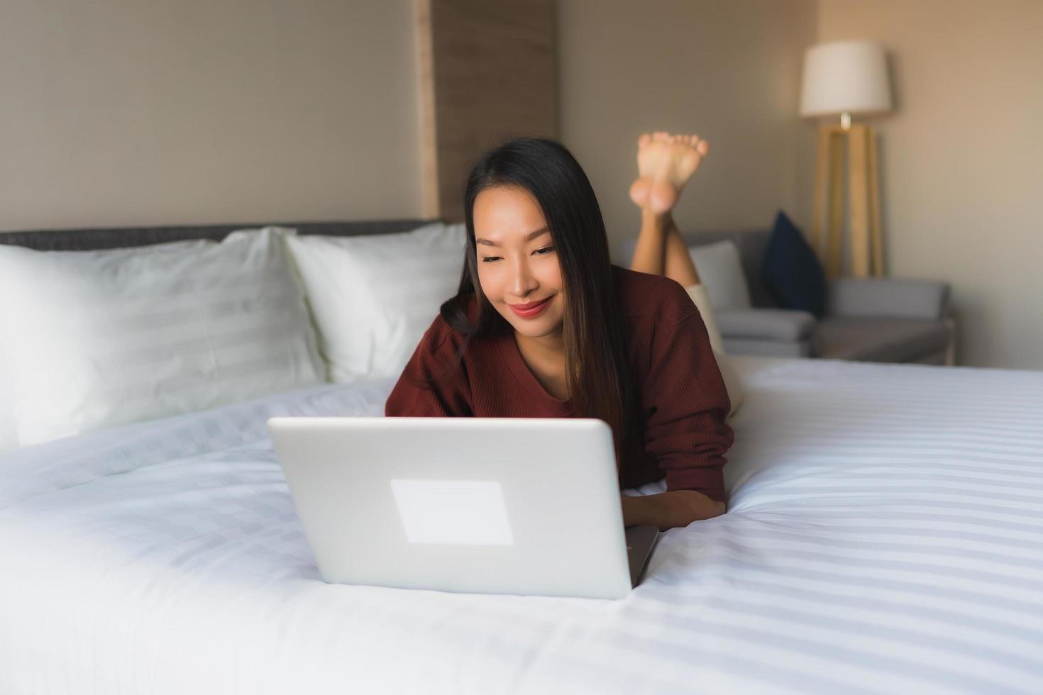 Portrait schöne junge asiatische Frauen mit Computer und Handy auf dem Bett foto