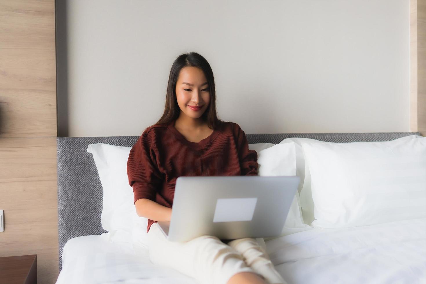 Portrait schöne junge asiatische Frauen mit Computer und Handy auf dem Bett foto