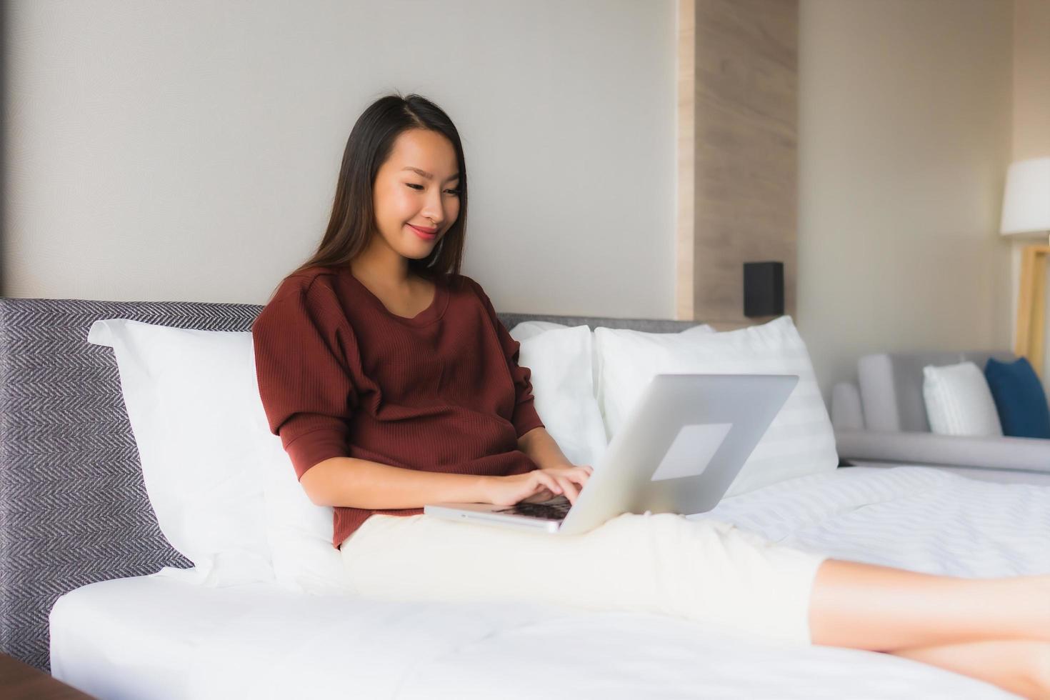 Portrait schöne junge asiatische Frauen mit Computer und Handy auf dem Bett foto