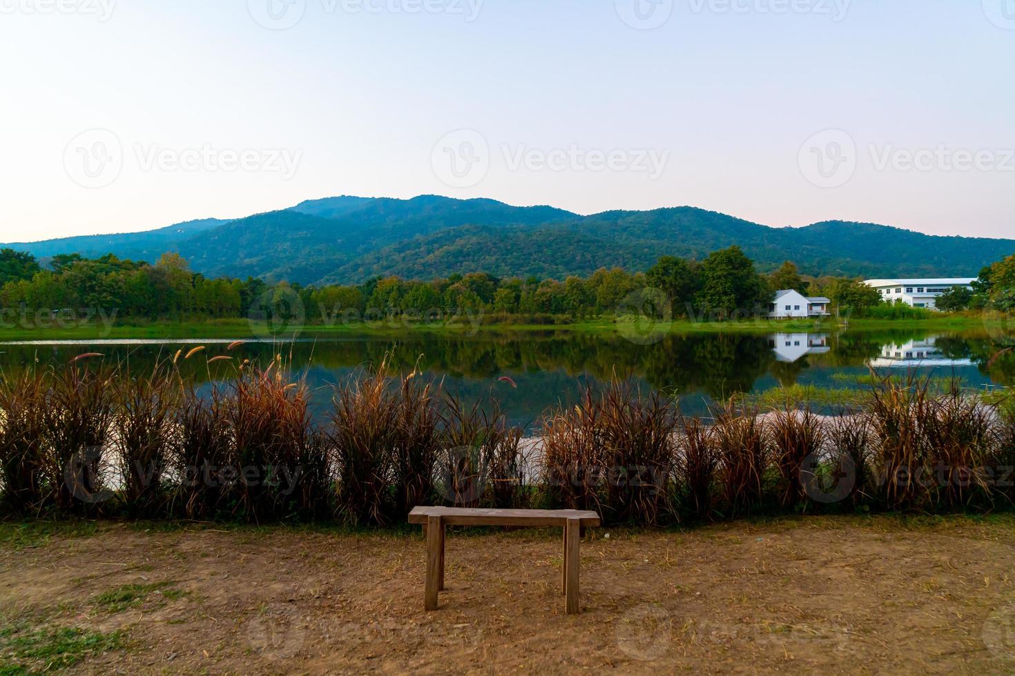 Holzbank mit einem wunderschönen See in Chiang Mai mit bewaldeten Bergen und Dämmerungshimmel in Thailand foto