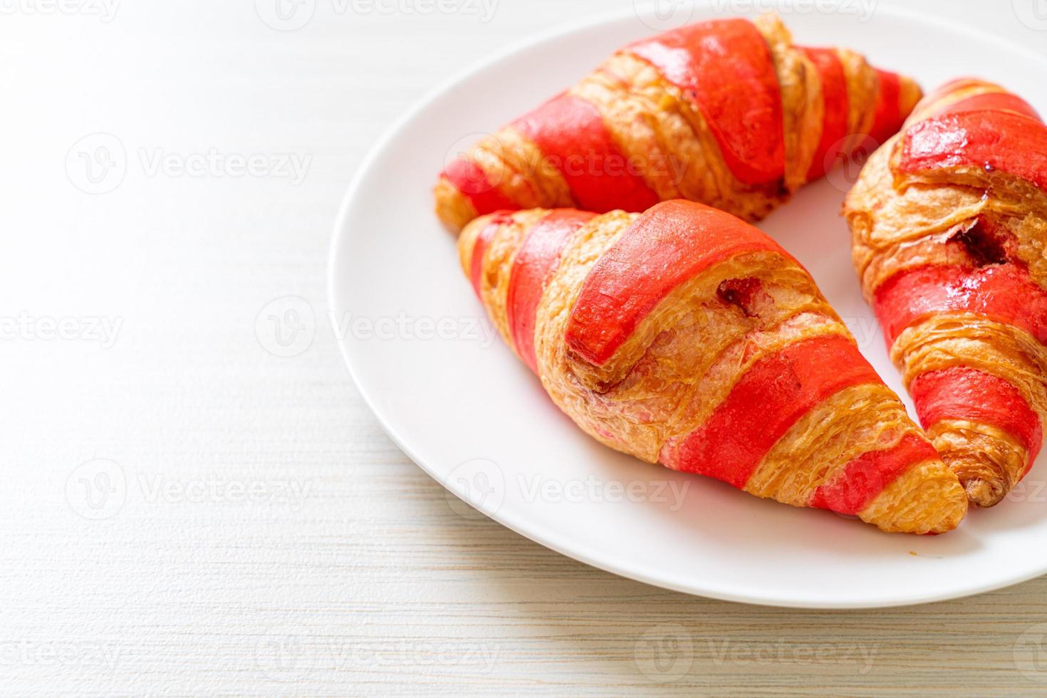 frisches Croissant mit Erdbeermarmeladesauce auf Teller foto