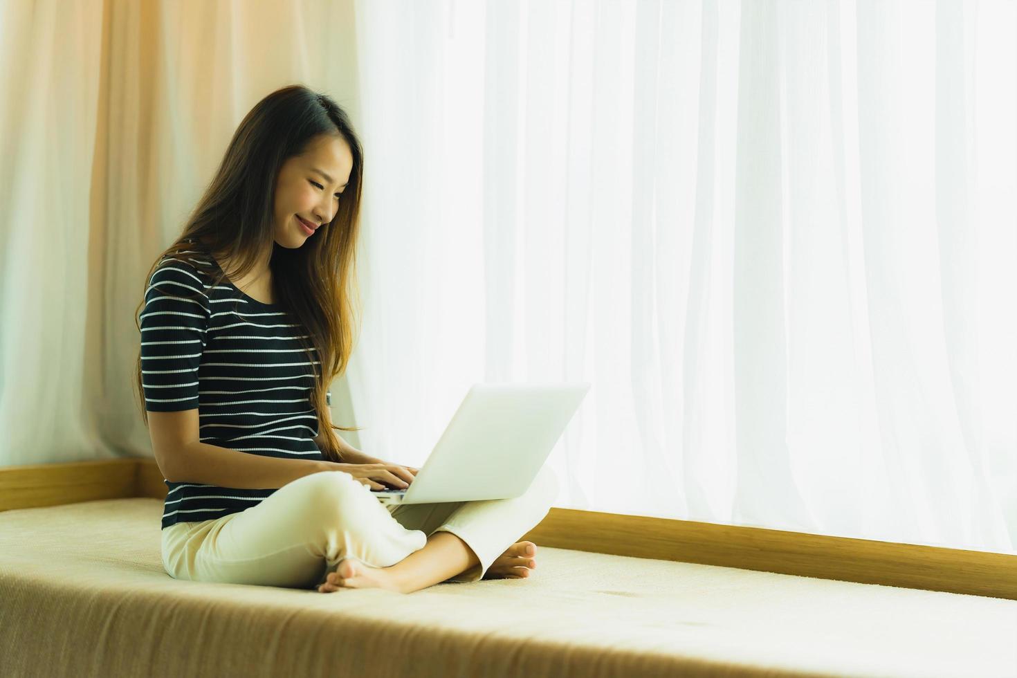 Porträt schöne junge asiatische Frau mit Computer-Notebook oder Laptop auf dem Sofa im Wohnzimmer foto