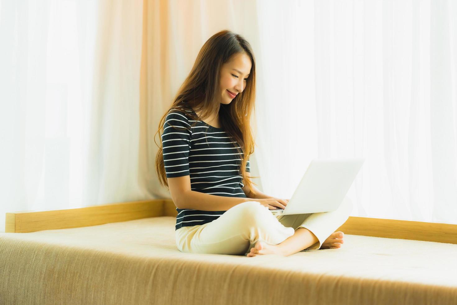 Porträt schöne junge asiatische Frau mit Computer-Notebook oder Laptop auf dem Sofa im Wohnzimmer foto