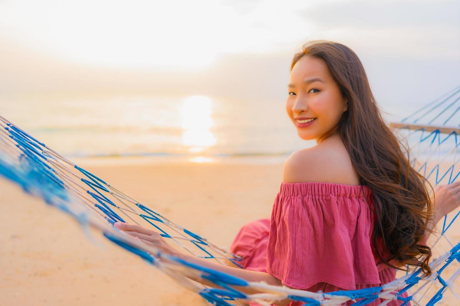 Porträt schöne junge asiatische Frau sitzt auf der Hängematte mit einem Lächeln glücklich in der Nähe von Strand Meer und Ozean foto