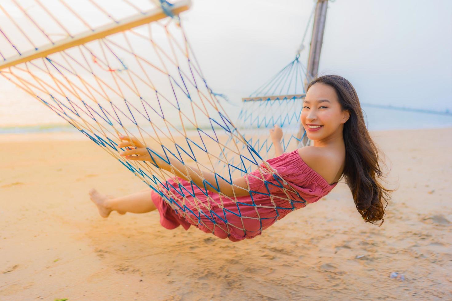 Porträt schöne junge asiatische Frau sitzt auf der Hängematte mit einem Lächeln glücklich in der Nähe von Strand Meer und Ozean foto