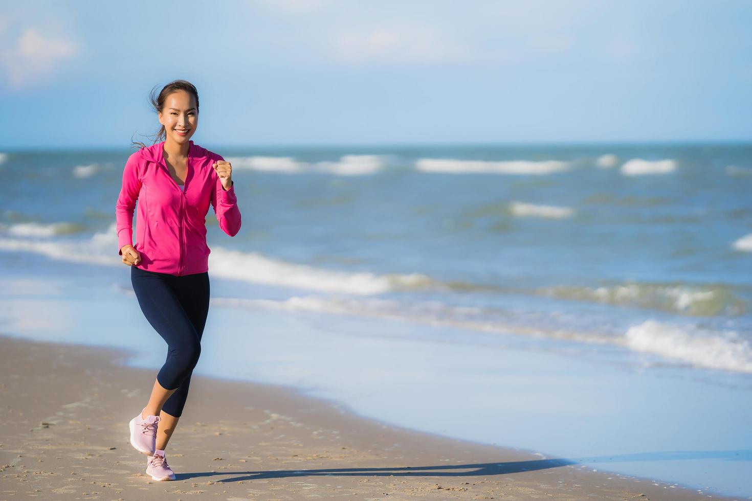 Porträt schöne junge asiatische Frau, die auf dem tropischen Naturstrand Meer Ozean läuft und trainiert foto