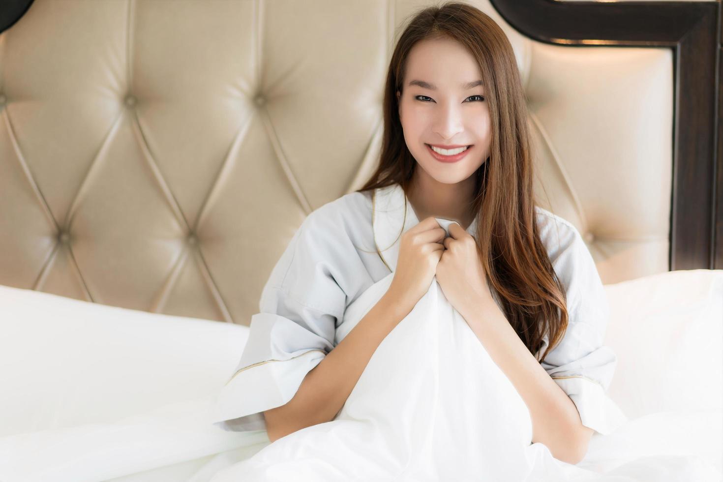 Porträt schöne junge asiatische Frau wacht glücklich auf und lächelt auf dem Bett im Schlafzimmerinnenraum foto