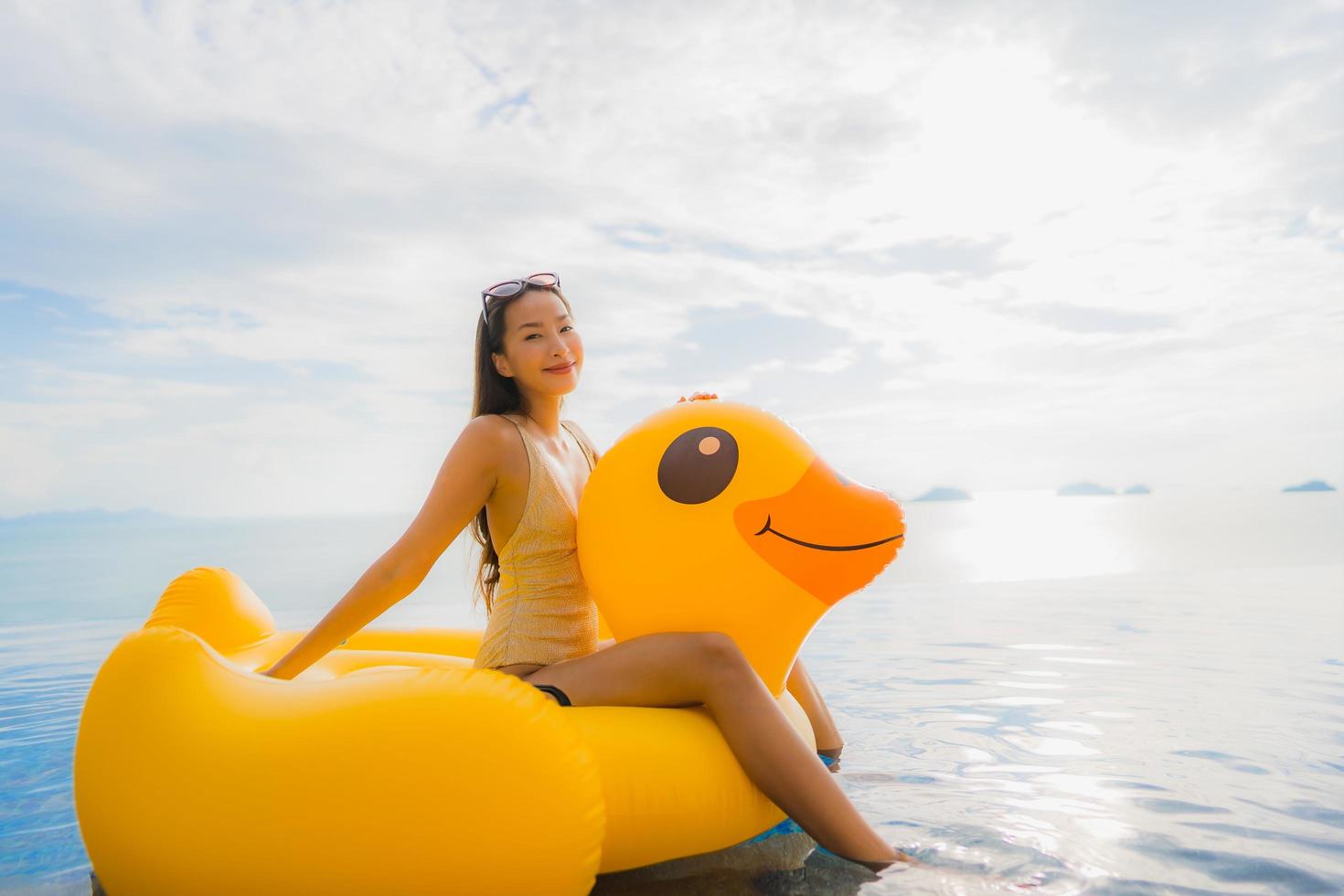 Porträt der jungen asiatischen Frau auf aufblasbarem Schwimmer gelbe Ente um den Außenpool im Hotel und Resort foto