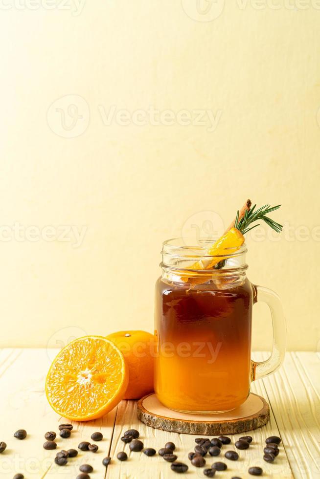 ein Glas eisgekühlter Americano-Schwarzkaffee und eine Schicht Orangen- und Zitronensaft, dekoriert mit Rosmarin und Zimt auf Holzhintergrund foto