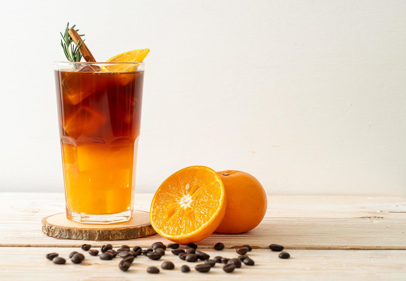 ein Glas eisgekühlter Americano-Schwarzkaffee und eine Schicht Orangen- und Zitronensaft, dekoriert mit Rosmarin und Zimt auf Holzhintergrund foto