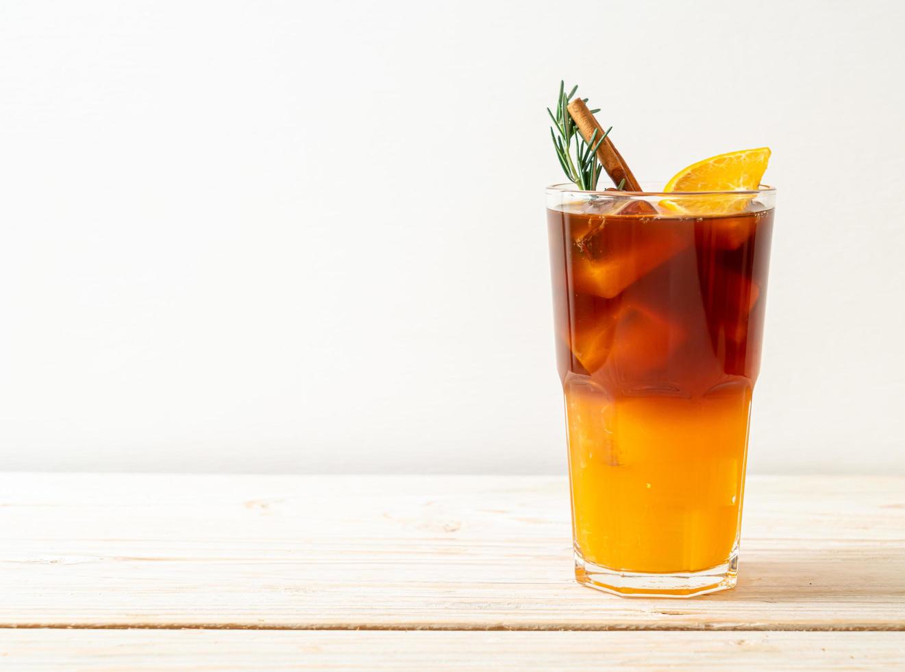 ein Glas eisgekühlter Americano-Schwarzkaffee und eine Schicht Orangen- und Zitronensaft, dekoriert mit Rosmarin und Zimt auf Holzhintergrund foto