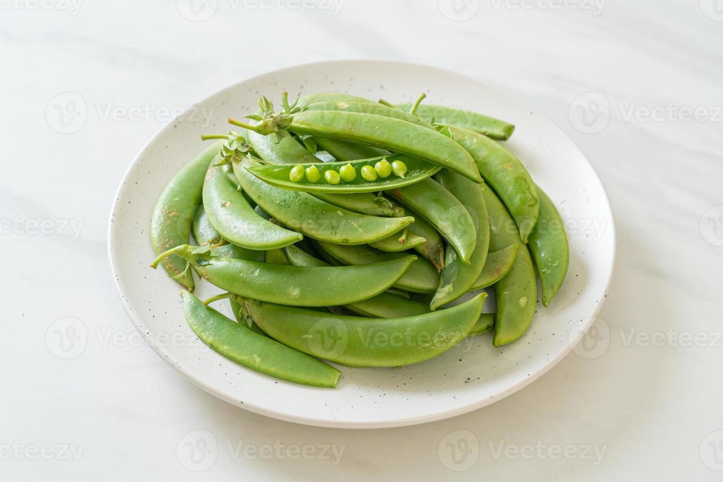 frische süße grüne Erbsen auf weißem Teller foto