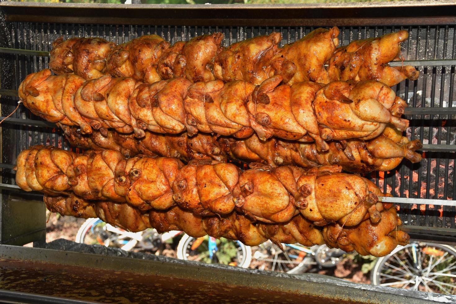 gebratene Hähnchen am Spieß über dem Feuer eines großen Grills gegrillt foto