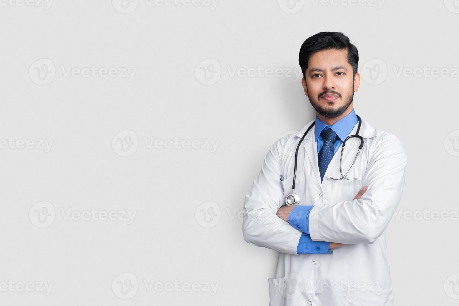 junger Arzt männliche Kreuzarme über isoliertem Hintergrund lächelnd foto