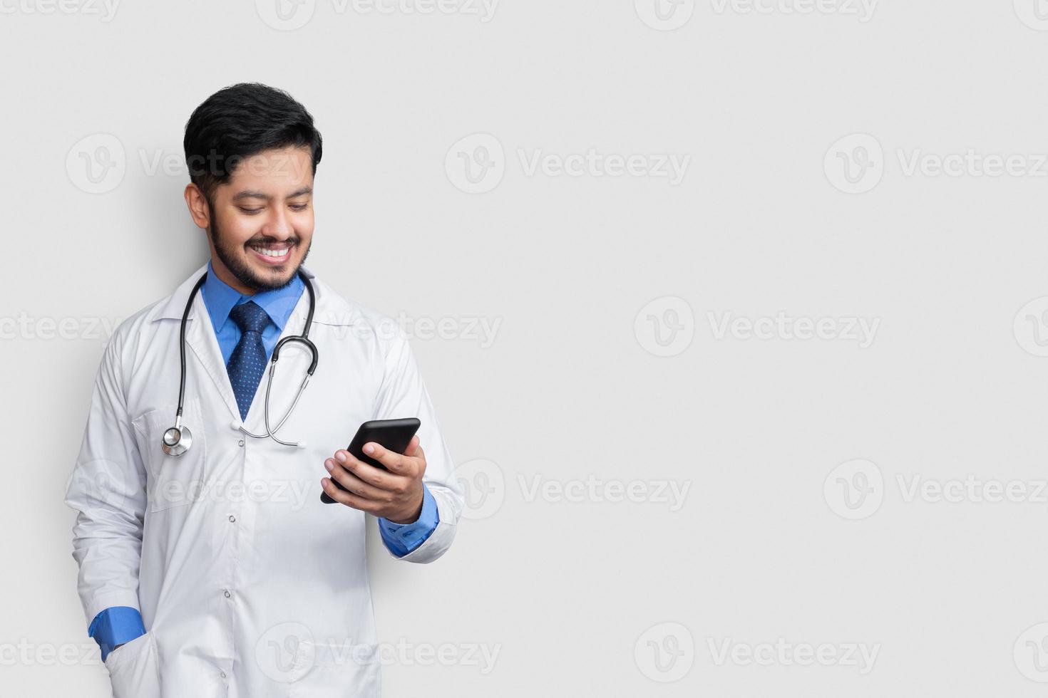 Arzt lächelt und schaut auf das Telefon. pakistanischer mann arzt technologie medizin zu hause. foto