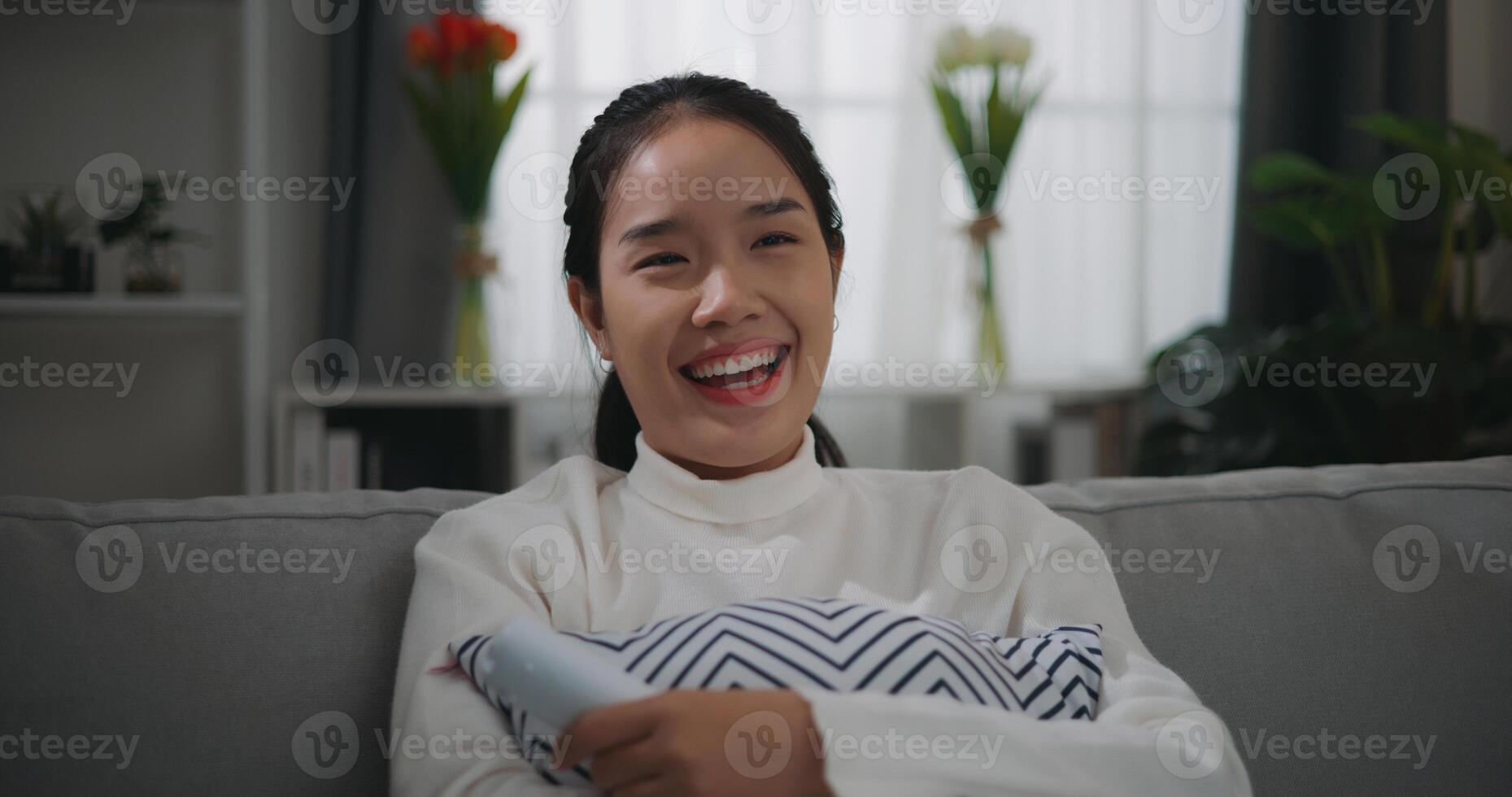glücklich jung asiatisch Frau Aufpassen ein Film auf Fernsehen während Sitzung auf das Sofa foto