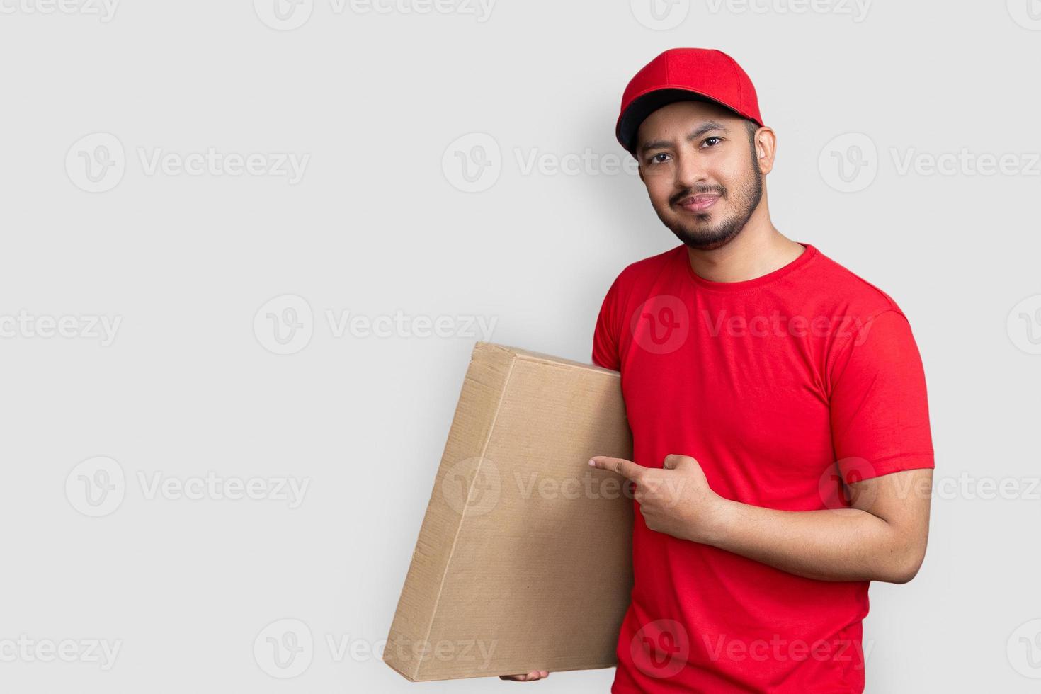 Lieferbote Mitarbeiter in roter Mütze leeres T-Shirt Finger Uniform halten leeren Karton isoliert auf weißem Hintergrund foto