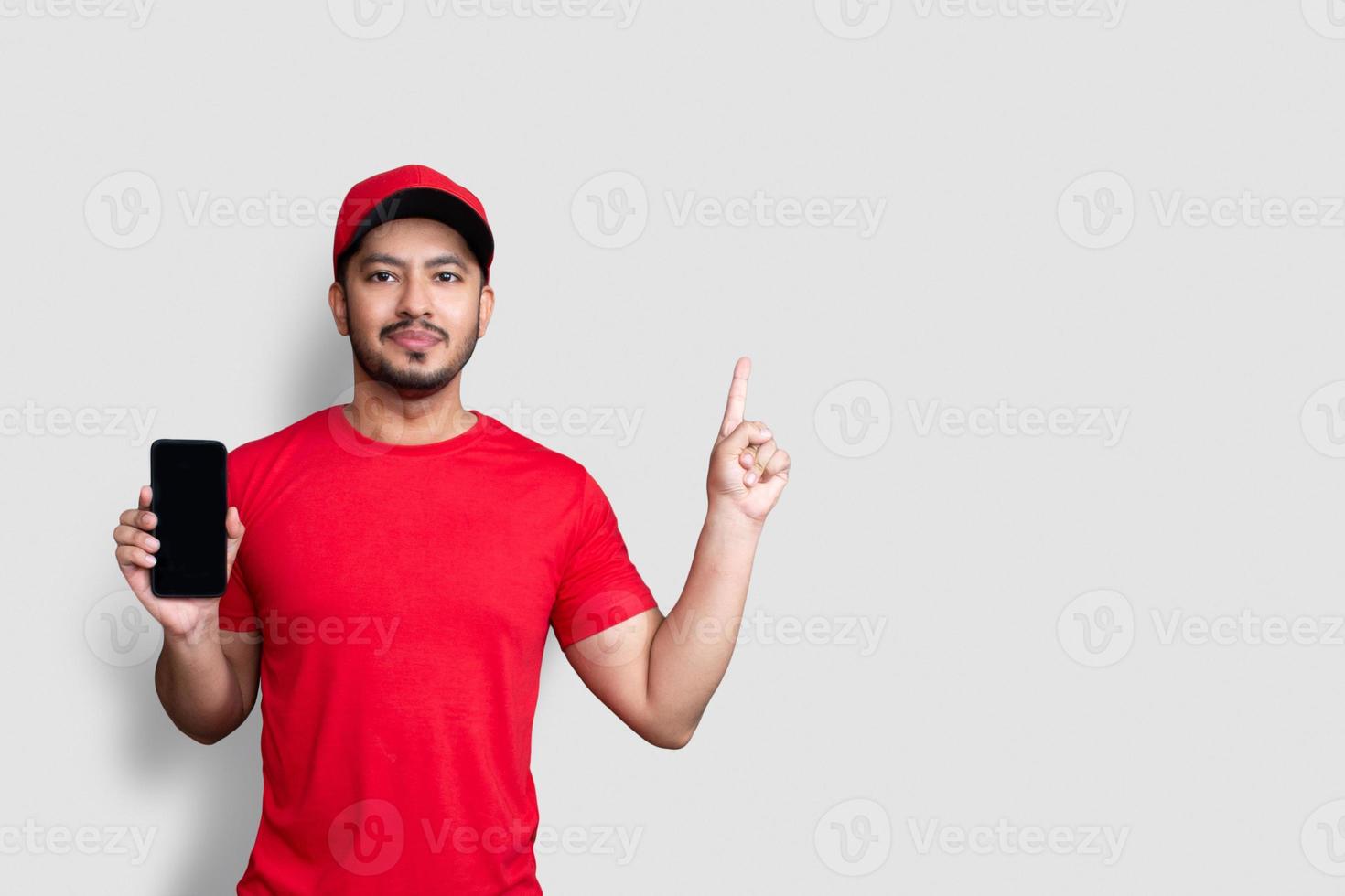 Lieferbote-Mitarbeiter in roter Kappe leeres T-Shirt-Uniform halten schwarze Handy-Anwendung isoliert auf weißem Hintergrund foto