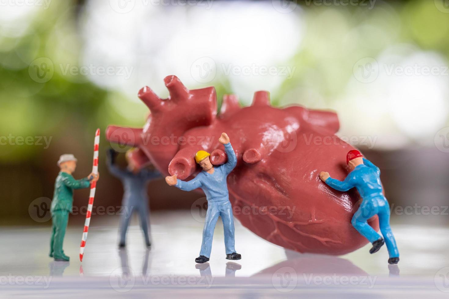 Miniaturmenschen-Arbeiterteam untersucht das Herz, hört auf einen Herzschlag und stellt eine Diagnose foto