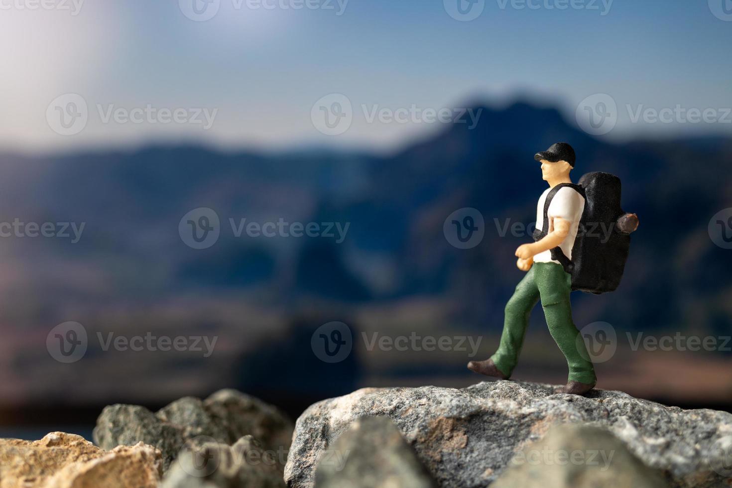 Miniaturreisender mit Rucksack, der auf den Felsen geht foto