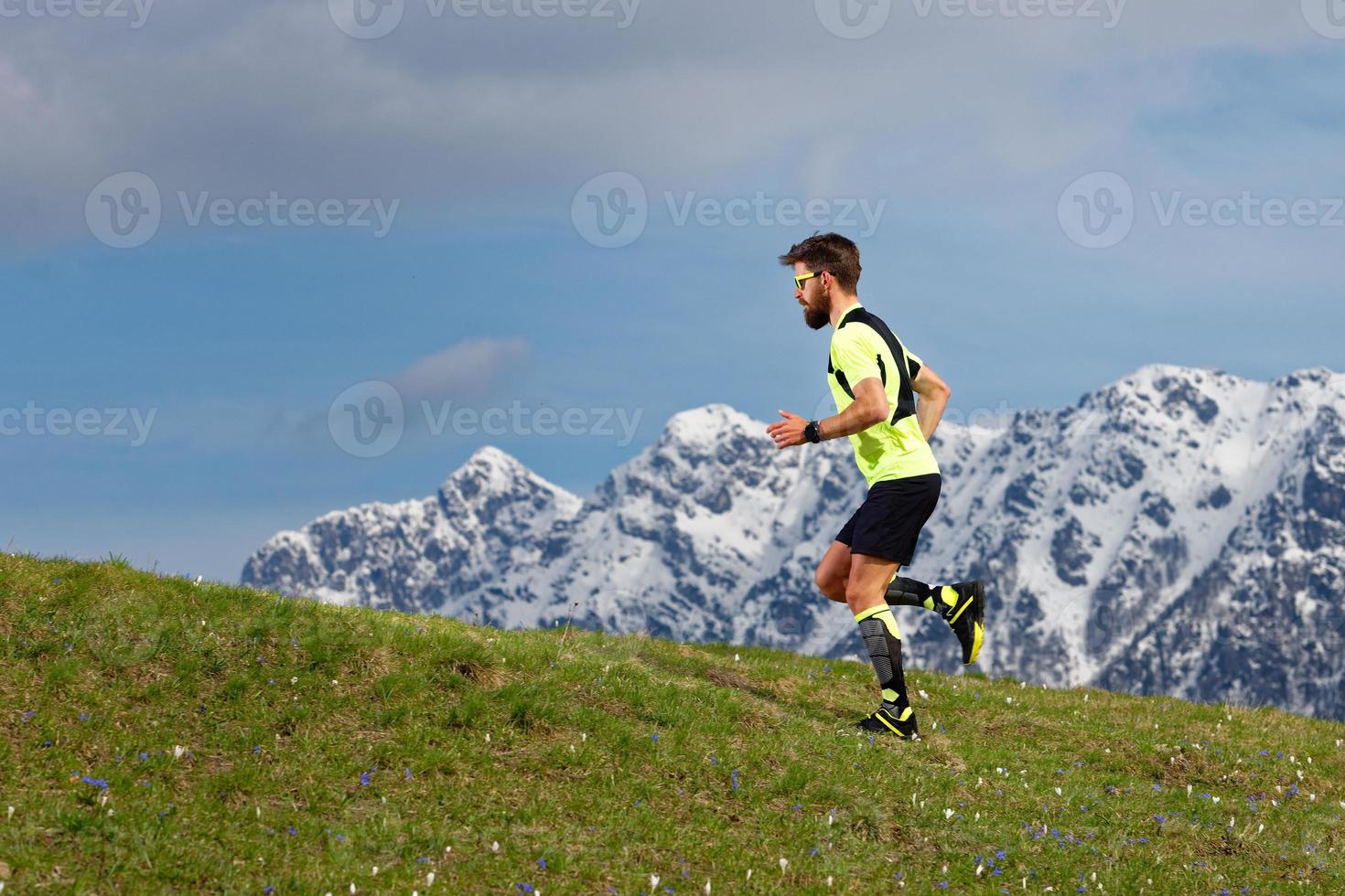 Skyrunning einen bärtigen Mann auf einer Frühlingswiese mit Schneebergen Hintergrund foto