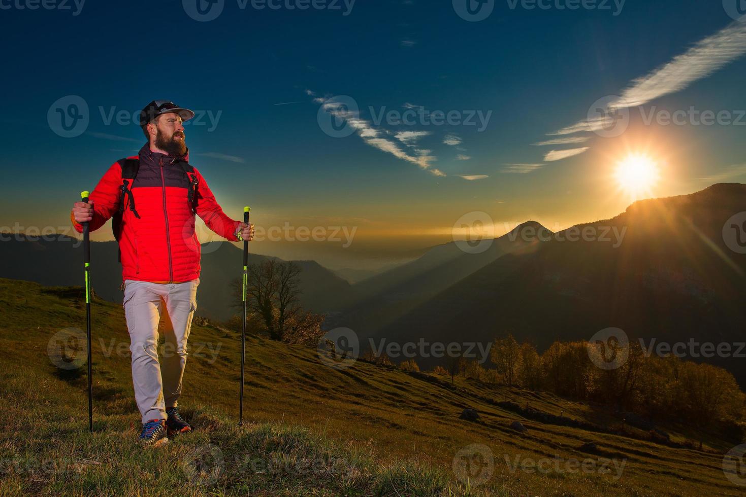 junger Mann mit Bart, der das Panorama beobachtet, ruht sich während einer Nordic Walking-Wanderung aus foto