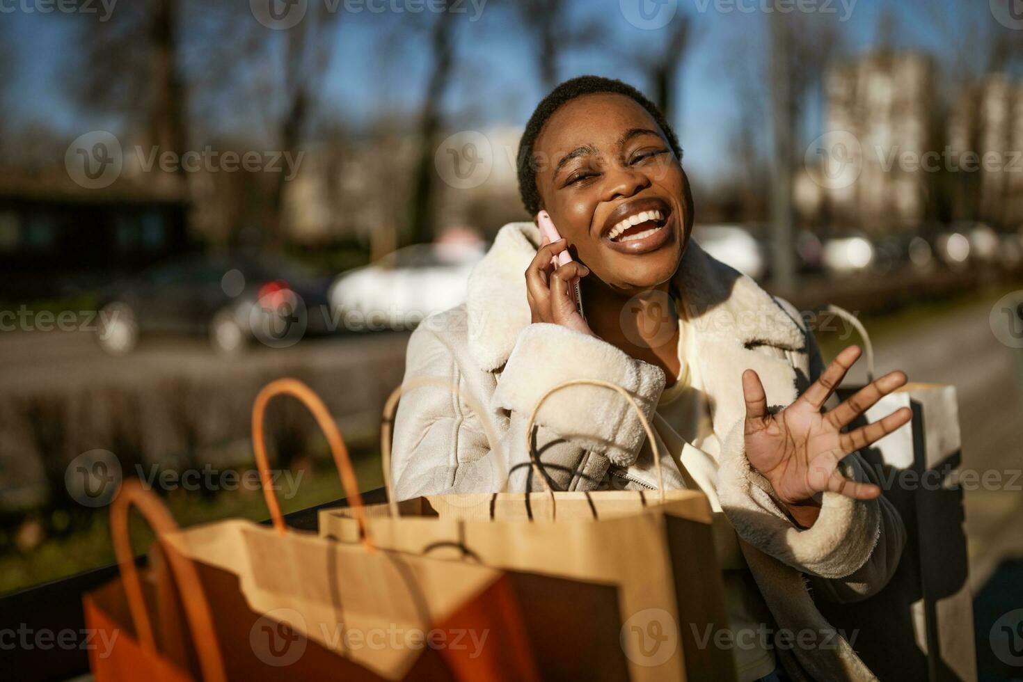 draussen Porträt von glücklich schwarz Frau. sie ist Sitzung auf Bank im das Straße nach Einkaufen. foto