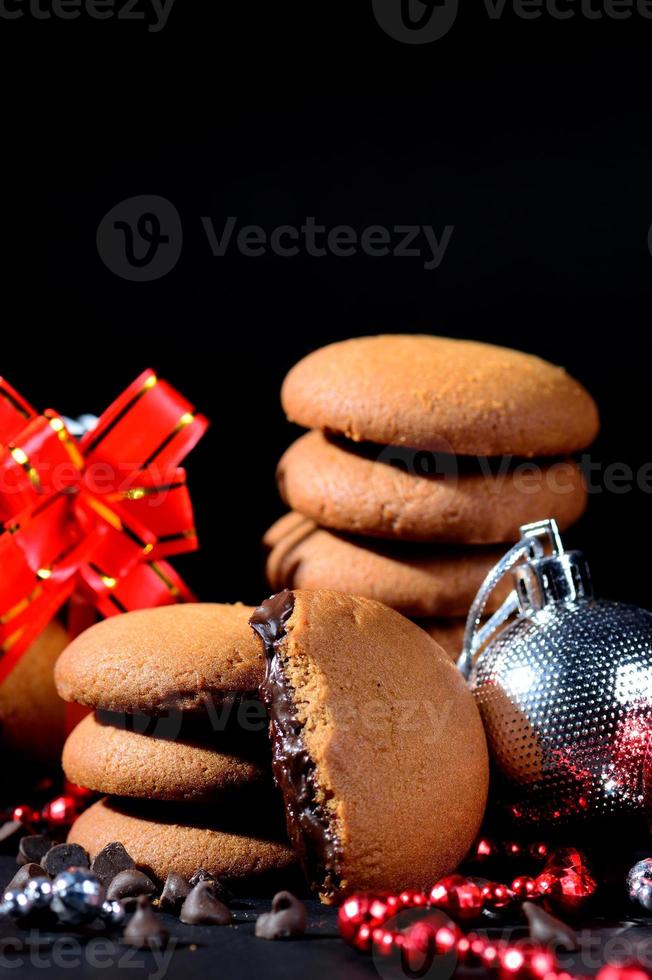 Kekse - Stapel köstlicher Sahnekekse gefüllt mit Schokoladencreme, verziert mit Weihnachtsschmuck auf schwarzem Hintergrund foto